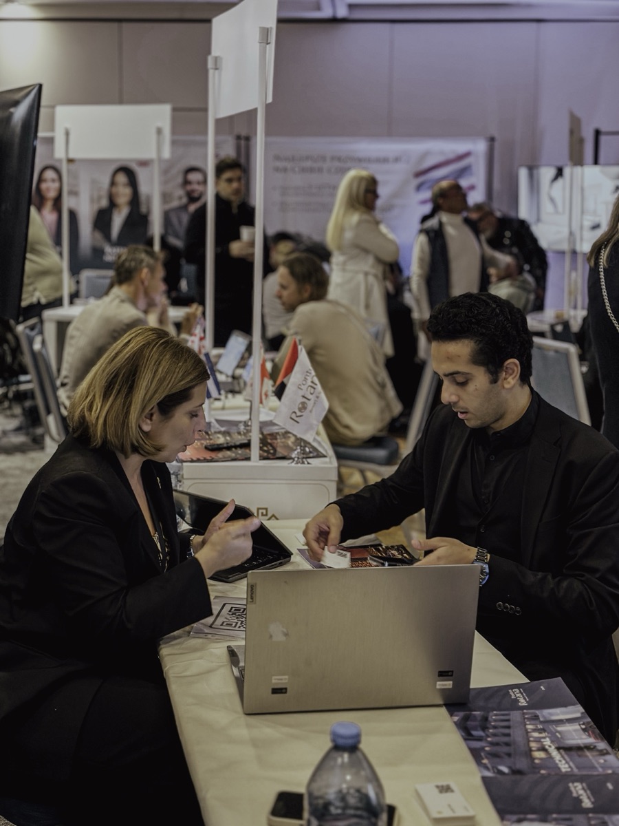 Two attendees at a B2B expo booth with small Polish and Egyptian flags on the meeting table.